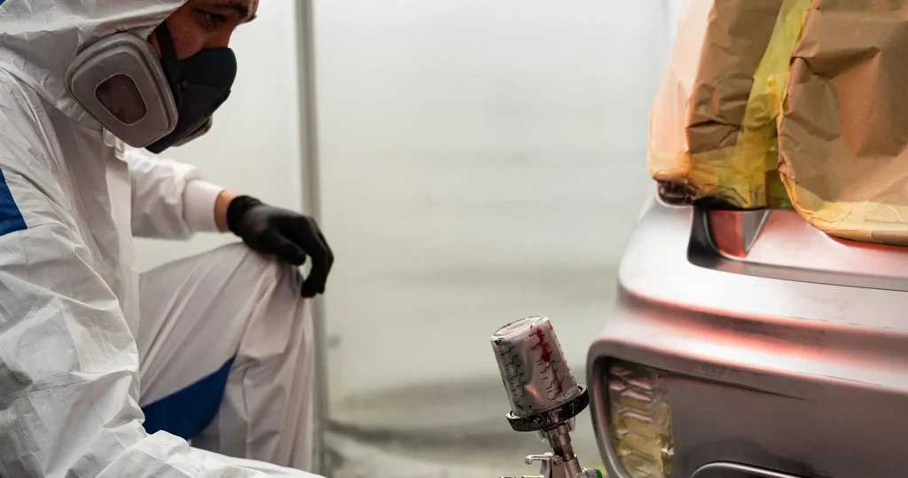 Painter spraying a masked rear bumper in the booth
